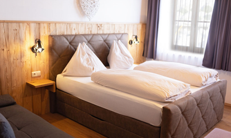 A cozy bedroom with a double bed and two pillows. The wooden paneling and soft lighting create an inviting atmosphere.