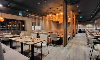 A modern restaurant with elegant wooden furniture and warm lighting. The atmosphere is inviting and stylish.