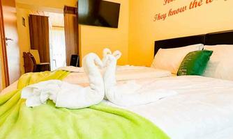 A cozy bedroom with a large bed and a green bedspread. A motivational quote hangs on the wall, and a television is installed.