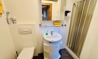 A modern bathroom with sink, toilet, and shower. The walls are bright and there are some bath towels and toiletries.