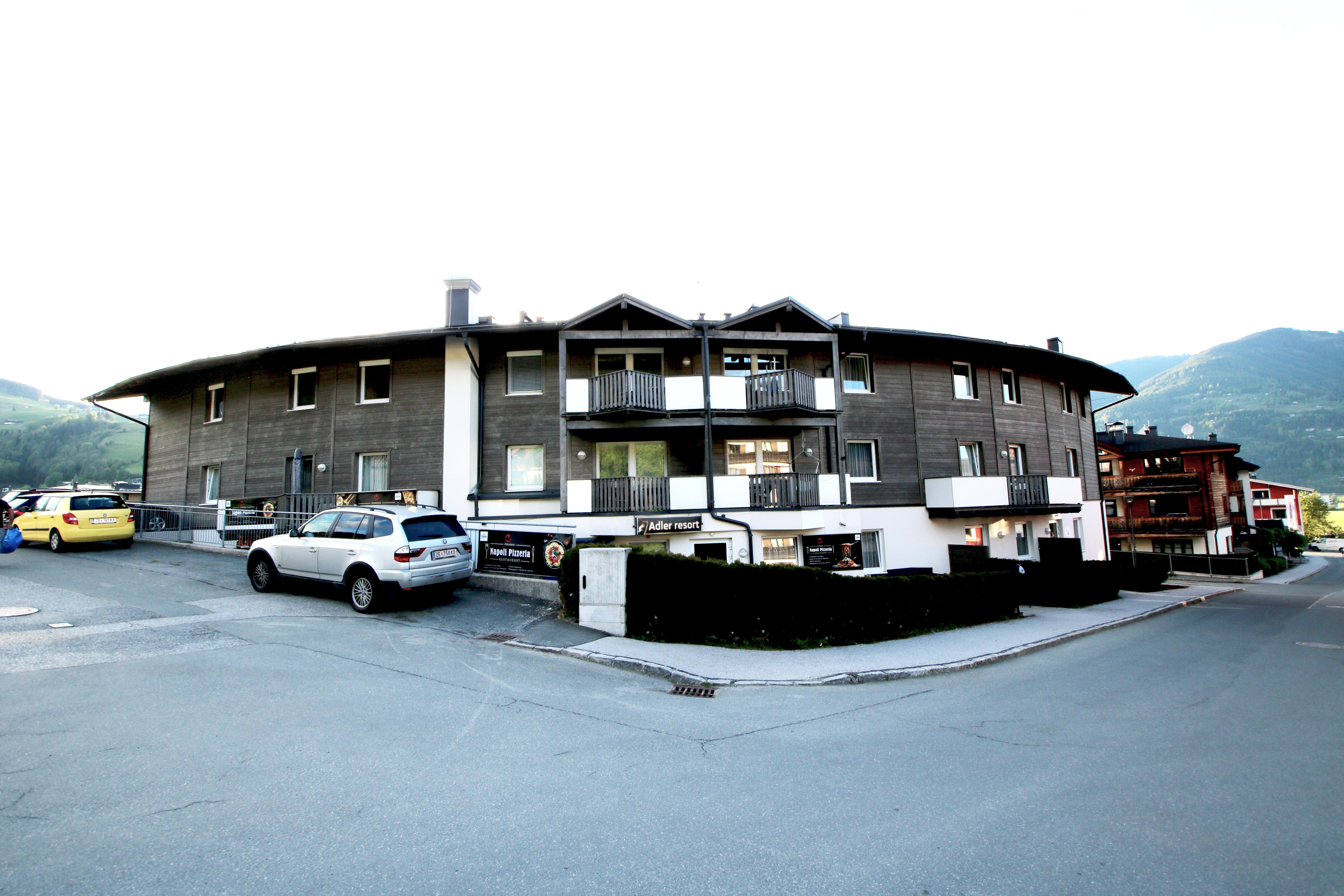 A modern, round building with apartments and parking spaces. Mountains are visible in the background.