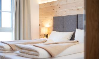 A cozy bedroom with a bright wood panel and a soft, gray headboard. The beds are invitingly decorated with warm blankets.