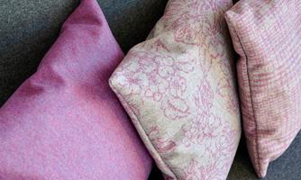 Three decorative cushions in different shades of pink on a gray couch. The cushions have varying textures and patterns.