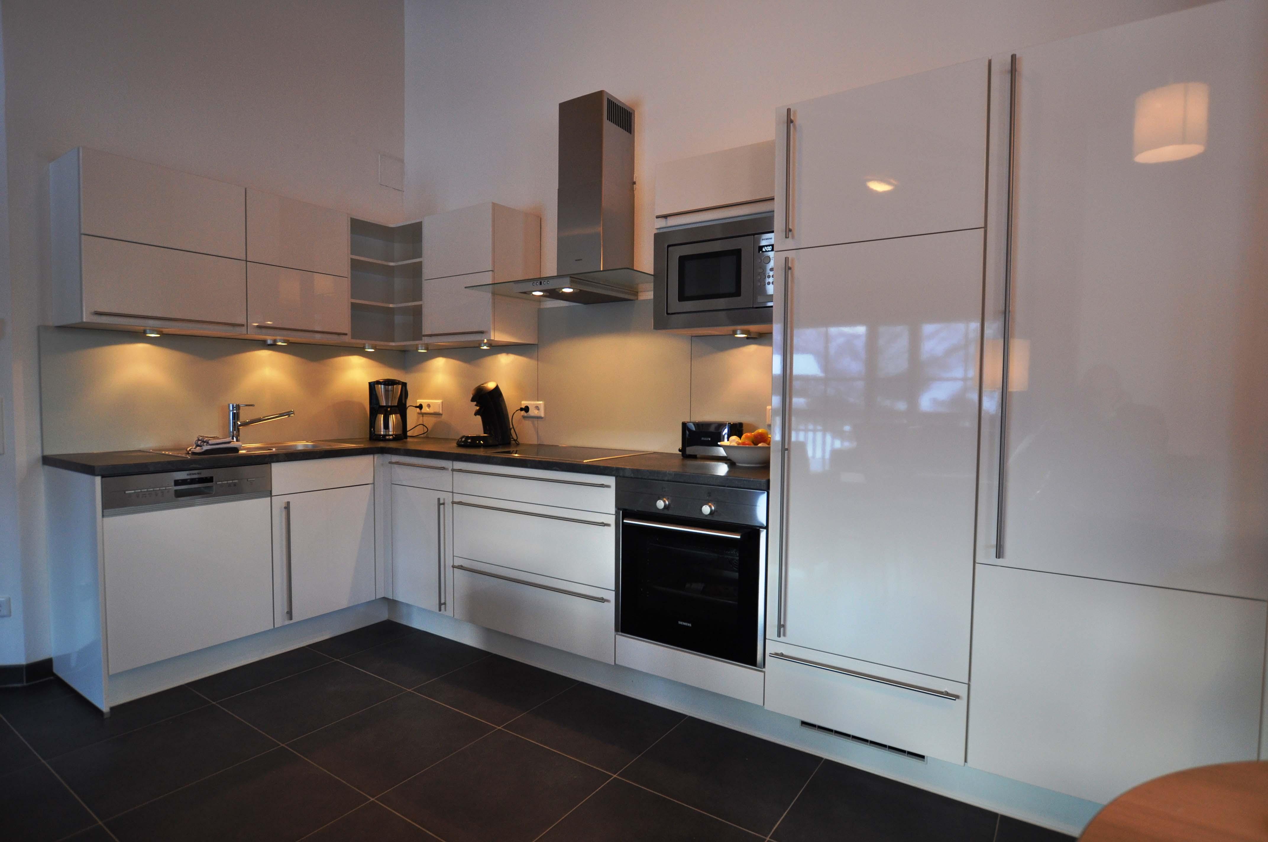 Modern kitchen with shiny white cabinets and a black stove. The lighting creates an inviting atmosphere.