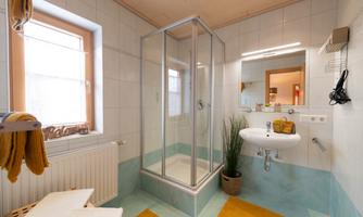 A modern bathroom with a shower cubicle and a sink. The walls are tiled in light colors, and there are orange mats on the floor.