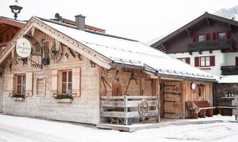 A cozy wooden house in the snow, surrounded by a serene winter landscape. The charm of alpine architecture is accentuated by the snow cover.