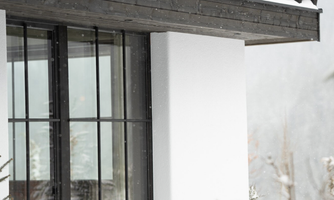 A modern house in the snow with large windows. The surroundings are wintry and quiet.