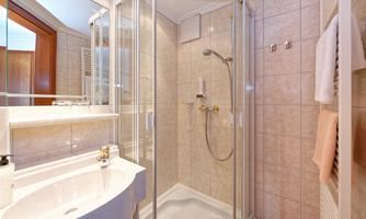 A modern bathroom with a shower, a sink, and bright tiles. Ample light comes in through the window.