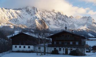 A picturesque mountain village in the snow, surrounded by majestic mountains. The sky is partly cloudy, giving the scene a serene atmosphere.