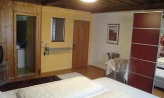 A simple room with two beds, wooden floor and a wooden ceiling. There is a wardrobe and a television as well as access to a bathroom.