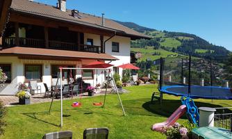 A cozy house with a well-maintained garden. The garden is equipped with swings, a trampoline, and a view of the surrounding hills.