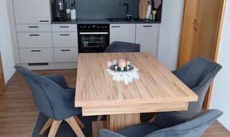 A modern kitchen with a wooden dining table and comfortable gray chairs. The room feels friendly and inviting.