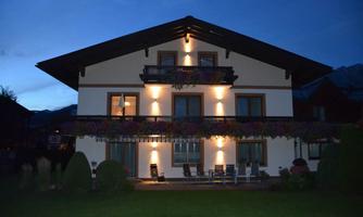 A modern house with a balcony, illuminated at dusk. The garden is well-maintained and offers a relaxed atmosphere.