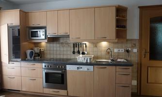 A modern kitchen with wooden cabinets and an electric stove. The appliances are well-organized and the countertop is tidy.