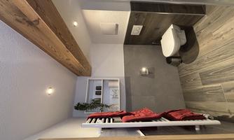 A modern bathroom with wooden details and elegant tiles. Red towels and a shower are also visible.