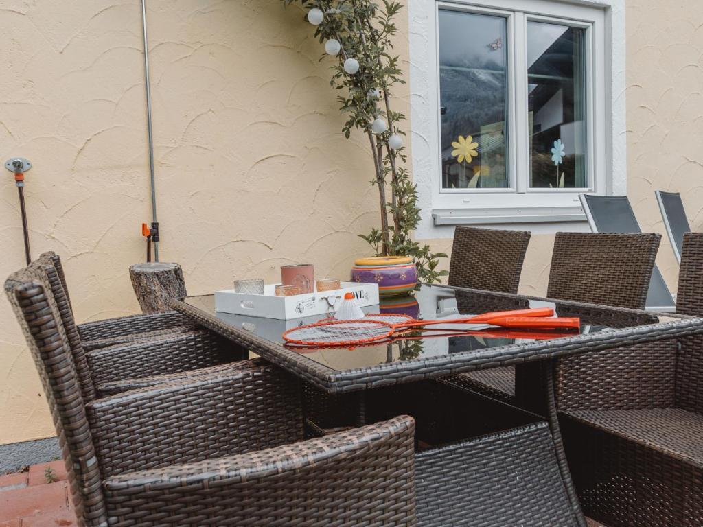 Seating group made of brown poly rattan with a glass top on a terrace, with game utensils and a flower in the background at the window.