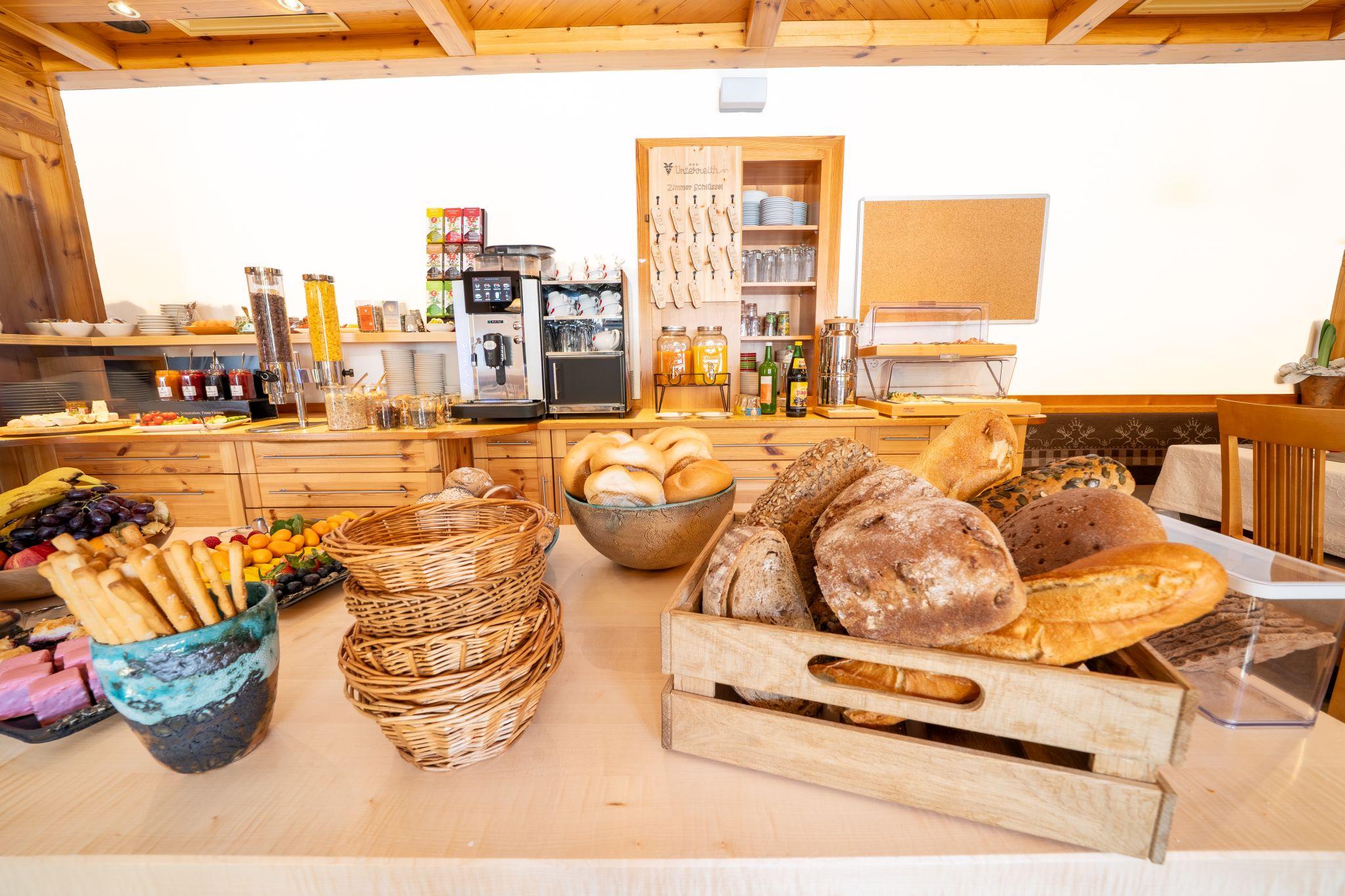 A buffet-style breakfast table with a selection of breads, pastries, and fresh fruits. In the background, drinks and a coffee machine are visible.