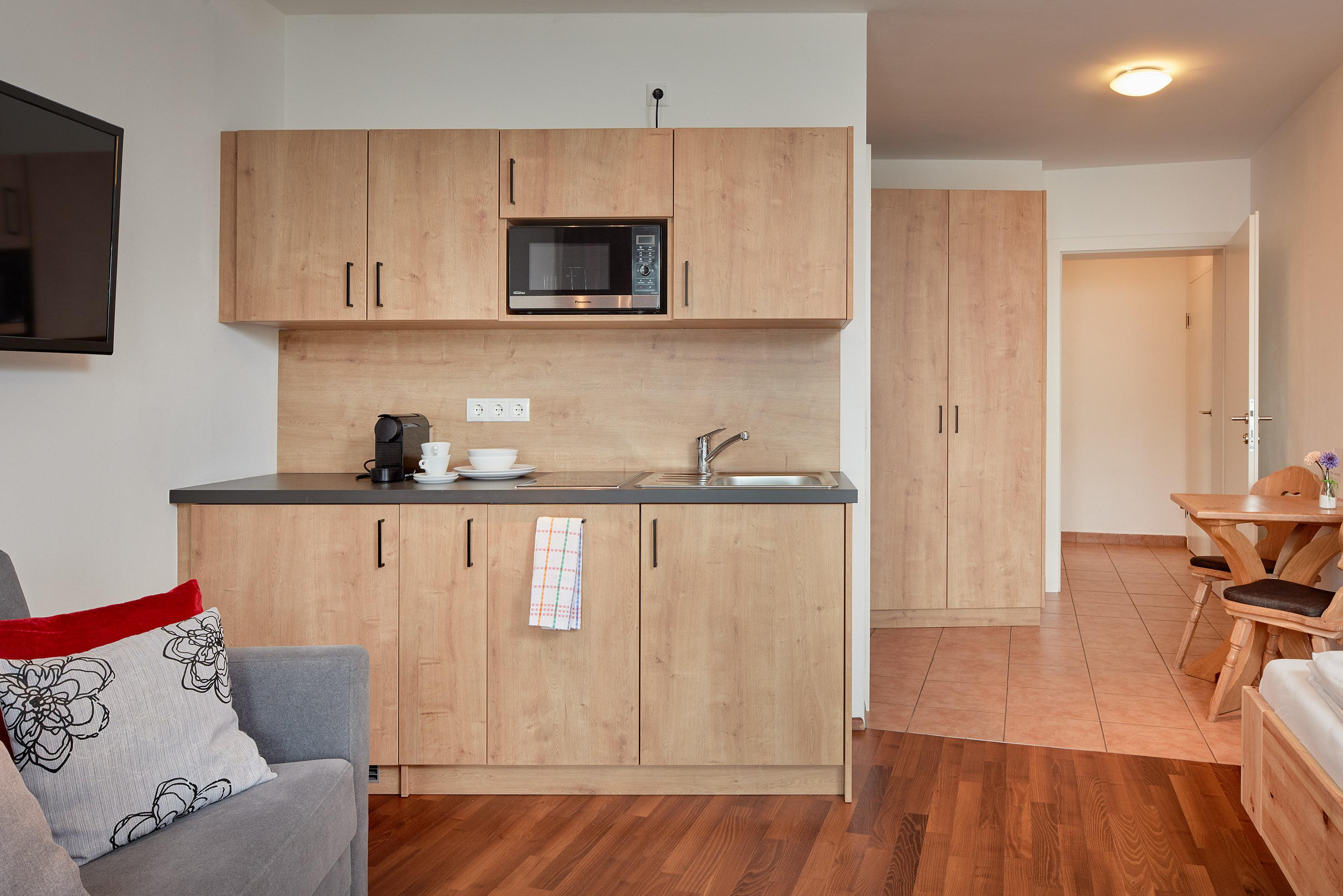 A modern kitchen with wooden cabinets, microwave, and cooking area. The space is bright and cheerfully furnished.