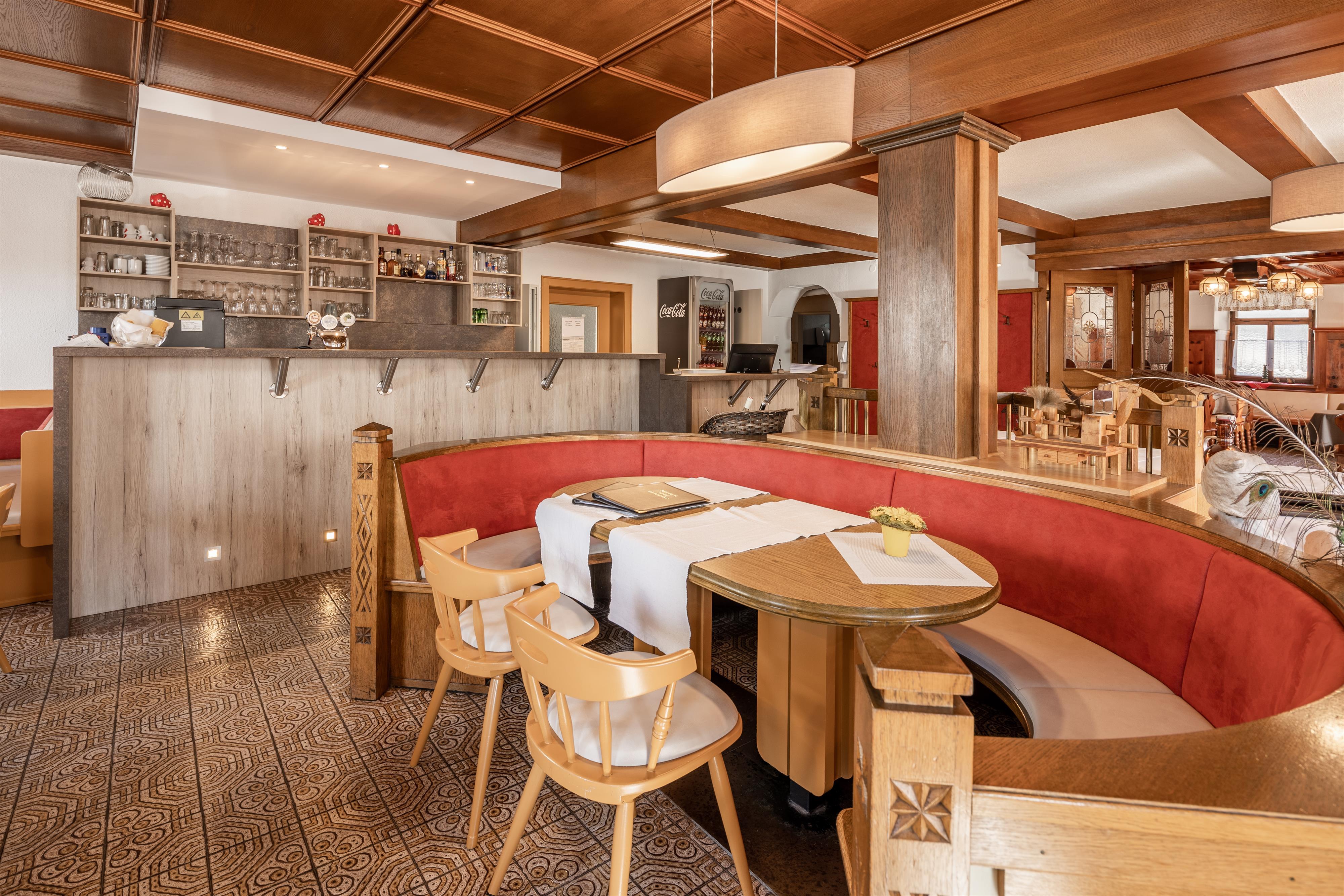 A cozy restaurant with a round table and a red bench. The wooden furniture and warm lighting create an inviting atmosphere.