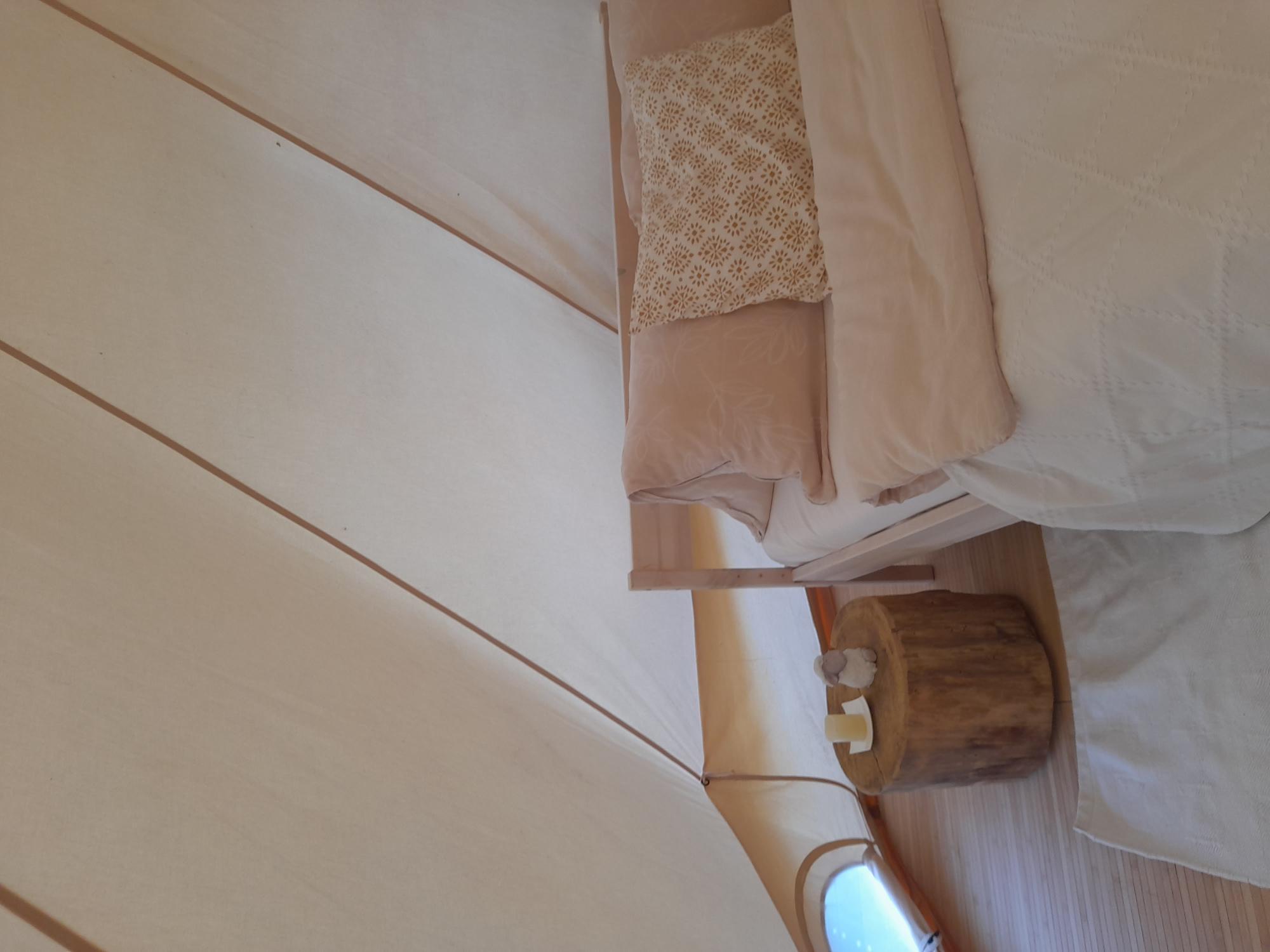 A cozy tent interior with a bed and a small wooden table. The decor is in soft colors and radiates tranquility.
