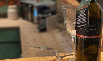 A bottle of wine stands on the counter next to two wine glasses. In the background, a cozy kitchen environment can be seen.