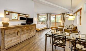 A modern living and bedroom with wooden floors. There is a bed, a television, and a dining area with a glass table.