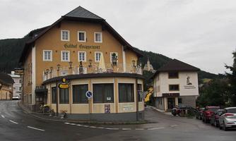 A traditional inn with several windows and a balcony. The street runs past other buildings in a mountainous area.