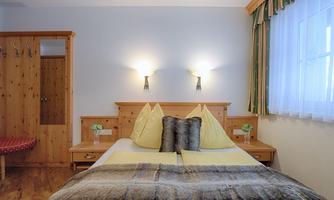 A cozy bedroom with a double bed and yellow pillows. The walls are light, and there are wooden cupboards and soft lighting.