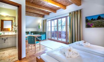 A cozy room with wooden ceilings and large windows. There is a bathroom and a seating area with a view of the outdoors.