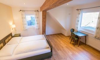 A cozy bedroom with a double bed and a small desk. Large windows provide plenty of daylight and a pleasant atmosphere.