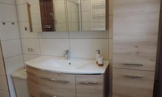 A modern bathroom with a wooden sink. The room is bright and well-lit, with a large mirror and a shower.
