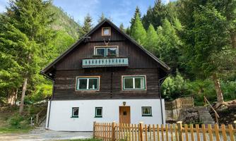 A large wooden house surrounded by trees and grass. The building has white walls and a balcony.