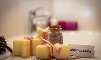 Handmade soaps in various shapes, accompanied by a small jar with ingredients. The presentation is lovingly decorated and highlights the naturalness of the products.