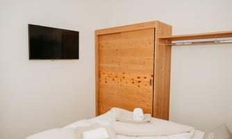 A cozy bedroom with a wooden wardrobe and a TV on the wall. The bedding is inviting and tidy.