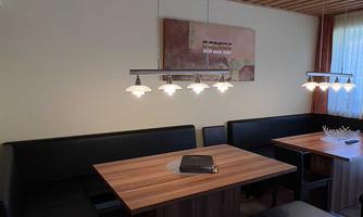 A modern dining room with a wooden ceiling and table groups. The furnishings consist of elegant benches and stylish lighting.