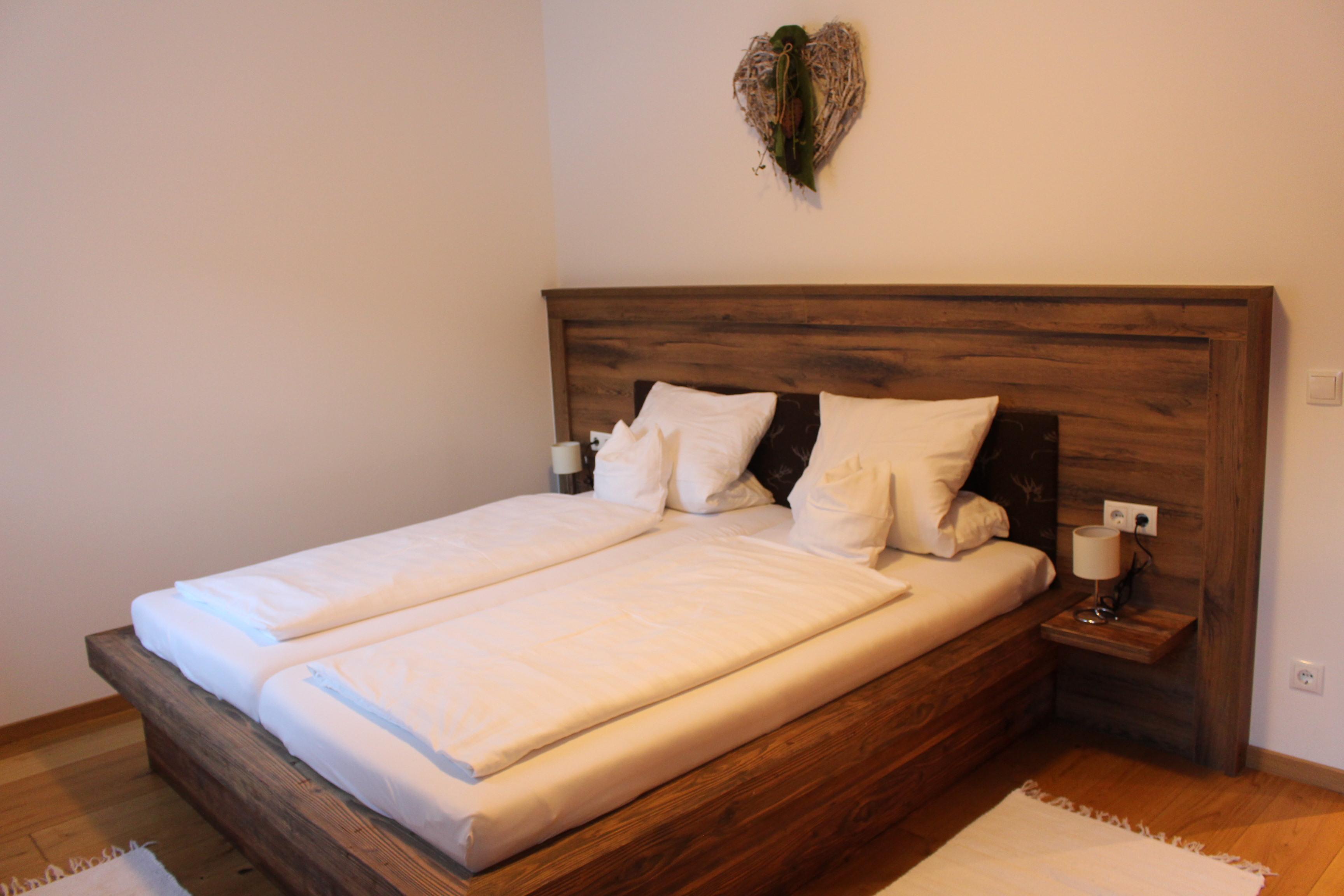 A modern bedroom with a wooden double bed. The walls are light, and there is a relaxing decoration.