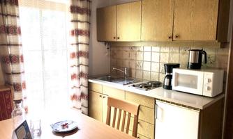 A bright kitchen with wooden cabinets and modern appliances. A dining table stands in the center, surrounded by chairs.