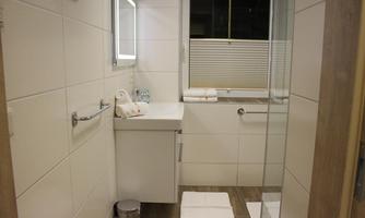 A modern bathroom with a white tiled wall and a glass shower area. Fresh towels and toiletries are placed on the countertop.