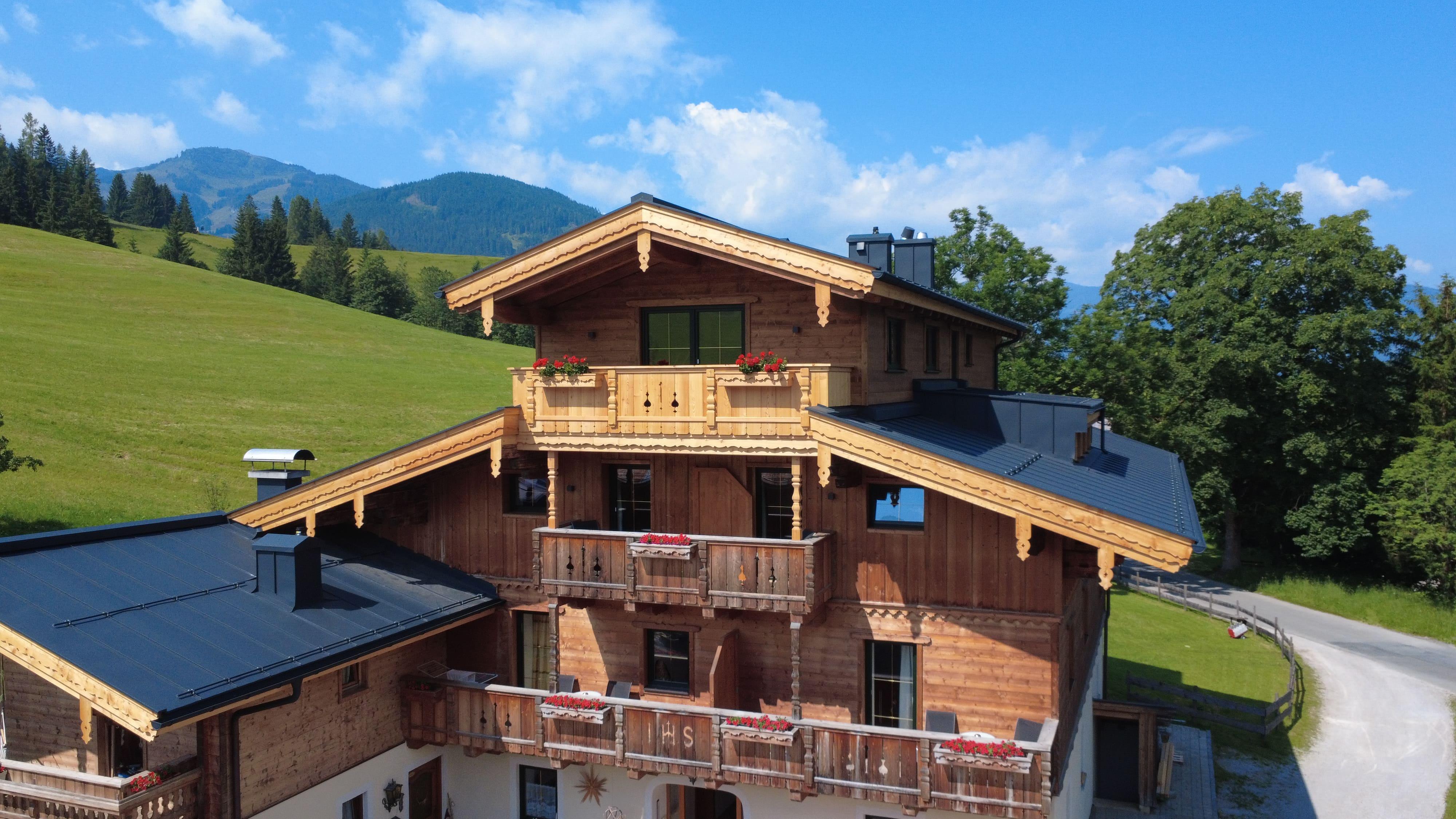 A beautiful wooden house amidst green hills and mountains. The sky is clear and sunny.