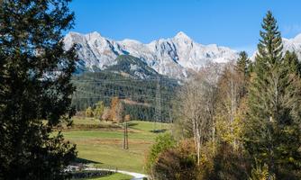 A picturesque landscape with high mountains in the background and lush green in the foreground. A narrow path winds through nature.