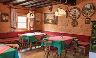 A cozy restaurant with wooden decor and traditional pictures. The tables are set with colorful tablecloths in green and red.