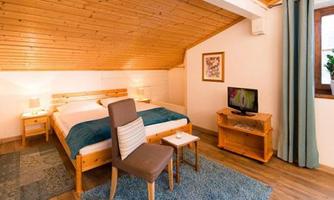 A cozy bedroom with a wooden ceiling and a large bed. A chair and a table complete the room, which looks bright and inviting.