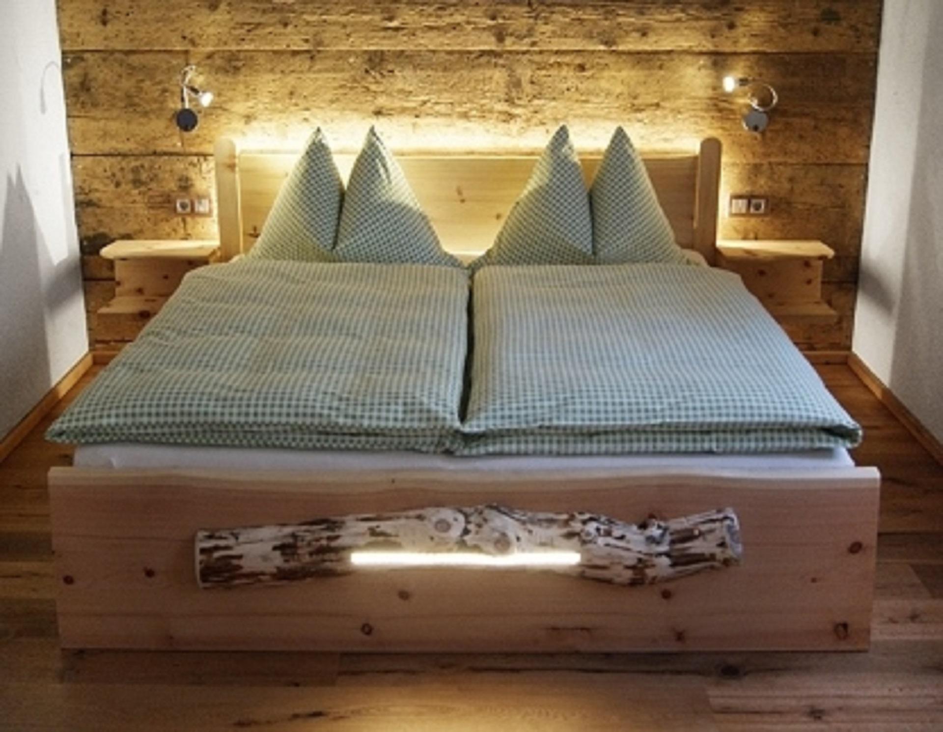A cozy room with a large wooden bed and green pillows. The warm wooden walls create an inviting atmosphere.