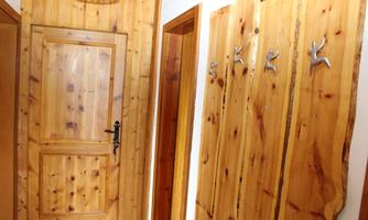 A cozy hallway with wooden walls and a wooden protective door. Silver hooks for jackets are hanging on the wall.