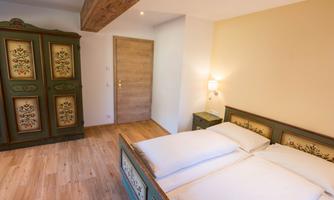 A cozy bedroom with a double bed and rustic furniture. The walls are softly painted, and there is comfortable storage in a decorative cupboard.