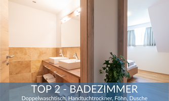 A modern bathroom with a double sink, towel warmer, and shower. Bright tiles and large windows create a friendly atmosphere.