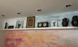 A wall shelf with various decorative objects, including picture frames and clocks. In the background, there is an abstract wall painting in soft colors.
