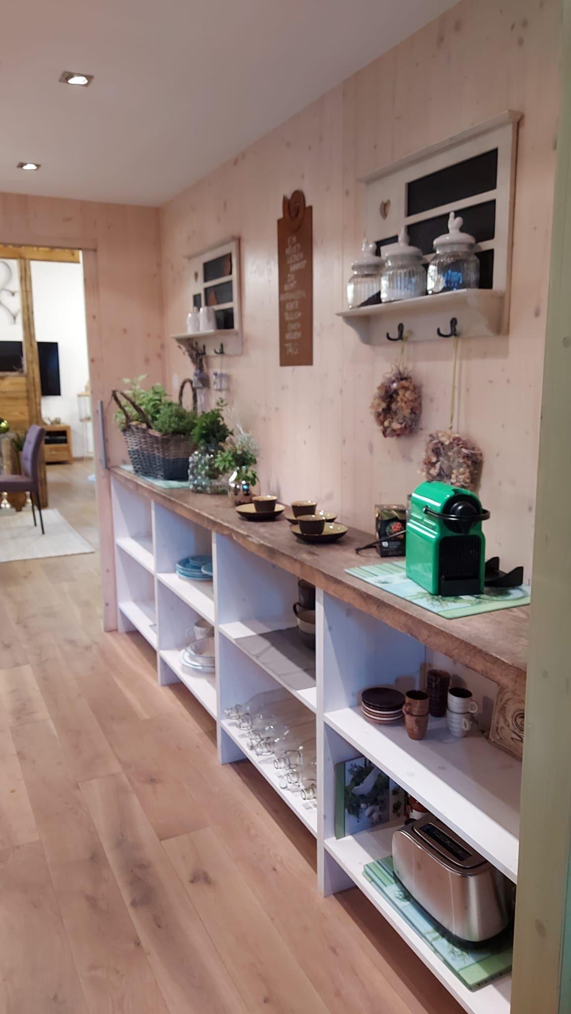 A cozy kitchen area with white shelves and wooden flooring. Decorative kitchen utensils and plants are on the countertop.