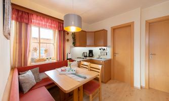 A cozy kitchen with a wooden table and chairs. The window lets in plenty of daylight and there is a small kitchenette.