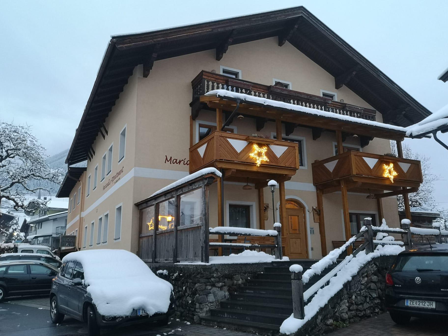 A beautiful building with two wooden balconies, adorned with poinsettias. The snow lies on the ground and on the roof, and the sky is gray.